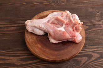 Raw turkey wing on a wooden cutting board on a brown wooden background. Side view, close up