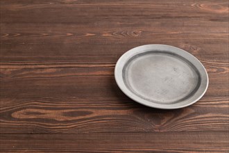 Empty gray ceramic plate on brown wooden background. Side view, copy space