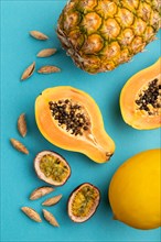 Ripe cut papaya, pineapple, melon, passion fruit, almonds on blue pastel background. Top view, flat