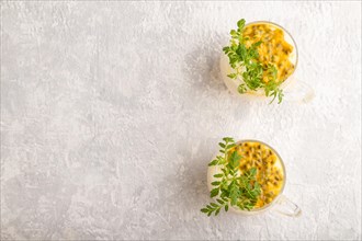 Yogurt with passionfruit and marigold microgreen in glass on gray concrete background. Top view,