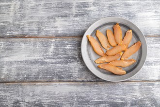 Salted meat on a wooden plate on a gray wooden background. Top view, flat lay, close up, copy space