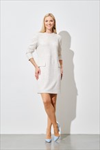 Sophisticated woman in textured white mini dress and blue heels posing against a white wall