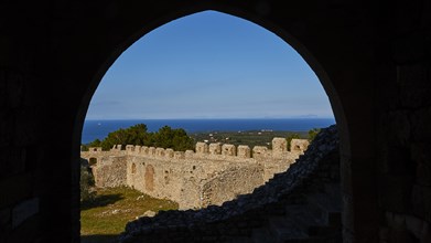 View through a stone arch onto historic fortress walls with blue sky and sea in the background,