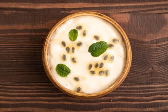 Yoghurt with granadilla and mint in wooden bowl on brown wooden background. top view, flat lay,