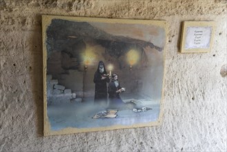 Mural painting with historical scene and information plaque on a cave wall, crypt, Aladja