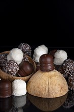 Stack of different chocolate kisses on a dark background, coconut half, reflection, copy space