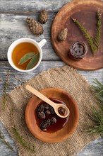 Pine cone jam with herbal tea on gray wooden background and linen textile. Top view, flat lay,