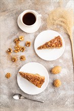 Walnut and hazelnut cake with caramel cream, cup of coffee on brown concrete background. top view,