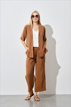 Cheerful blonde woman showcases a modern summer casual outfit. The loose brown suit and white inner