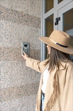 Vertical Side view of unrecognizable woman wearing a hat pushing the button of the intercom of