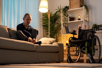 Low angle view portrait of a depressed disabled man sitting alone in the sofa at home