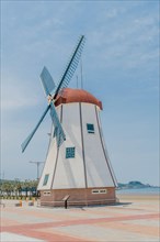Windmill at Chunjangdae Beach on sunny day with hazy blue sky in background in South Korea