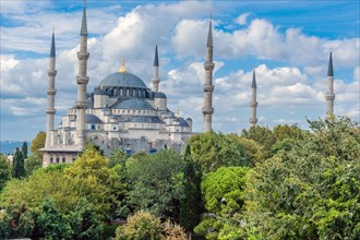 Hagia Sophia Mosque under cloudy blue sky with lush trees in foreground in Istanbul, Turkiye