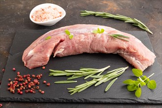 Raw pork meat with herbs and spices on slate cutting board on black concrete background. Side view,