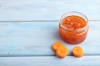 Carrot jam with cinnamon in glass jar on blue wooden background. Side view, copy space