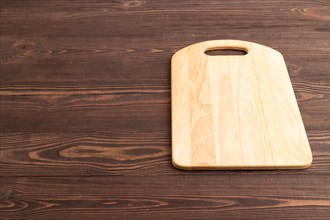 Empty rectangular wooden cutting board on brown wooden background. Side view, copy space