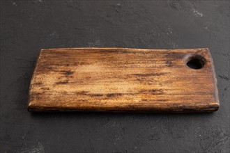 Empty rectangular wooden cutting board on black concrete background. Side view, close up