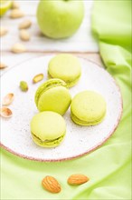 Green macarons or macaroons cakes with cup of coffee on a white wooden background and green linen