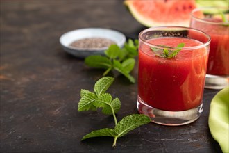 Watermelon juice with chia seeds and mint in glass on a black concrete background with green
