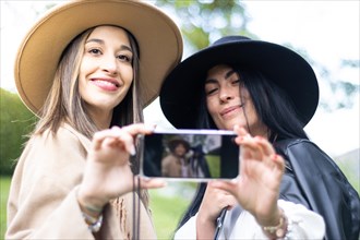 Front view of two stylish friends both grabbing a cell phones to take a selfie