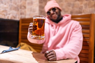 Cool african man toasting with a glass of beer sitting in a bar