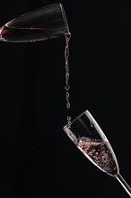 Rose champagne is poured from one champagne glass into another against a black background
