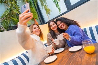 Dynamic shot of three women taking a selfie while drinking coffee in a cafeteria