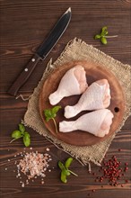 Raw chicken legs with herbs and spices on a wooden cutting board on a brown wooden background and