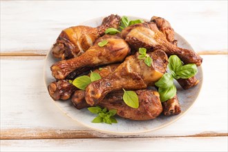 Smoked chicken legs with herbs and spices on a ceramic plate on a white wooden background. Side