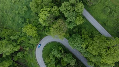 Blue car driving on serpentine road through green landscape, drone shot, Upper Bavaria, Bavaria,