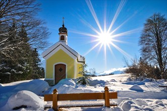 Backlit photograph of the snow-covered Maria Chapel on the humpback meadows of Werdenfelser Land