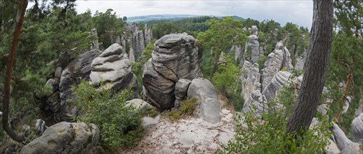 A panoramic view over bizarre rock structures surrounded by forest under a partly cloudy sky,
