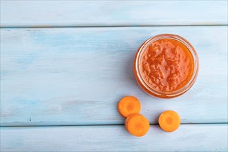 Carrot jam with cinnamon in glass jar on blue wooden background. Top view, flat lay, copy space