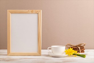 Wooden frame with oatmeal cookies yellow narcissus and coffee cup on beige pastel background. side