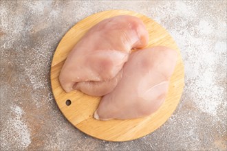 Raw chicken breast on a wooden cutting board on a brown concrete background. Top view, flat lay,