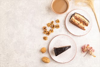 Chocolate biscuit cake with caramel cream and walnuts, cup of coffee on gray concrete background.