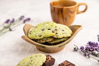 Green cookies with chocolate and mint on leaflike ceramic plate with cup of coffee on gray concrete