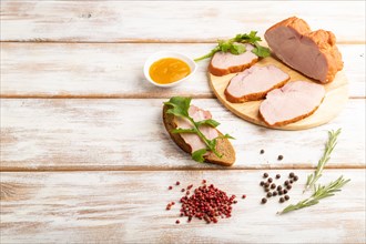 Smoked pork ham on cutting board with pepper and herbs on white wooden background. Side view, copy
