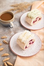Roll biscuit cake with cream cheese and jam, cup of coffee on brown concrete background and orange