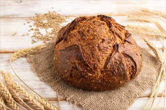 Fresh homemade golden grain bread with ears of wheat and rye on white wooden background and linen