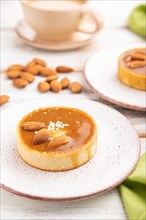 Sweet tartlets with almonds and caramel cream with cup of coffee on a white wooden background and