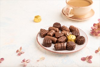 Chocolate candies with cup of coffee and hydrangea flowers on a white concrete background. side
