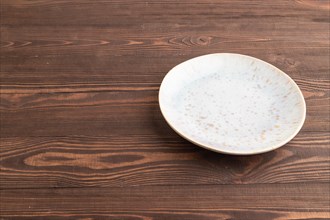 Empty blue and gold ceramic plate on brown wooden background. Side view, copy space