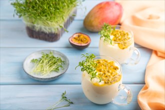 Mango yogurt with passionfruit and cilantro microgreen in glass on blue wooden background with