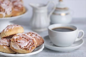 Coffee break with cinnamon buns next to a coffee cup, cream jug and sugar bowl in the background