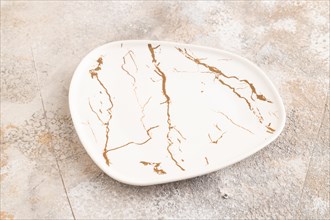 Empty white with golden pattern ceramic plate on brown concrete background. Side view, copy space