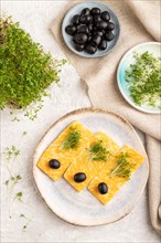 Marble cheese with olives and watercress microgreen on gray concrete background and linen textile.