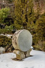 Decorative stone carved Korean drum at Buddhist temple in front of evergreen trees in South Korea