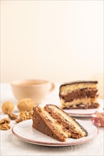 Chocolate biscuit cake with caramel cream and walnuts, cup of coffee on gray concrete background.