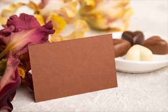Brown business card with chocolate candies and iris flowers on gray concrete background. side view,